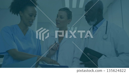 Reviewing patient information three staff wearing lab coats in hospital corridor, with blue folder 135624822