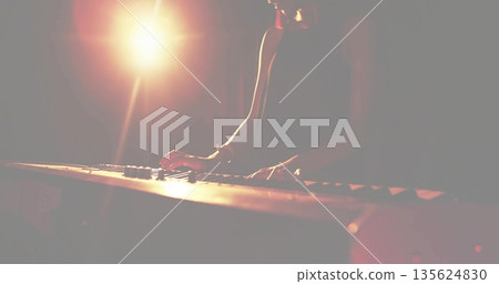Female musician wearing sleeveless top playing electric keyboard on dark stage, with spotlight 135624830