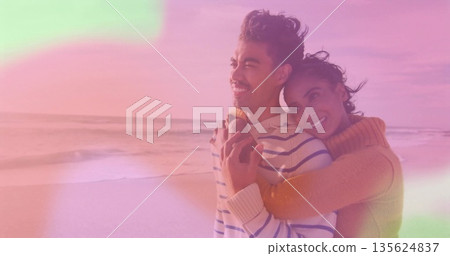 Hugging couple wearing mustard turtleneck and blue striped sweater on sandy beach, sunset glow Hugging couple wearing mustard turtleneck and blue striped sweater on sandy beach, sunset glow 135624837