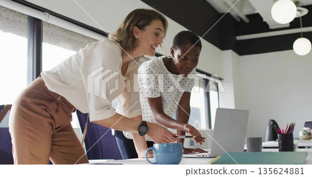 Collaborating adult women pointing at laptop screen in modern office, with coffee mug notebook 135624881