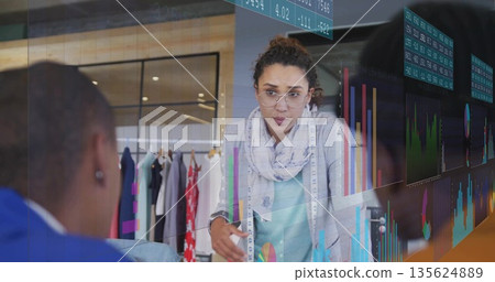 Presenting woman with glasses and measuring tape at studio, showing chart overlays, clothing rack Presenting woman with glasses and measuring tape at studio, showing chart overlays, clothing rack 135624889