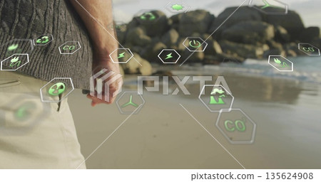 Standing man wearing grey sweater beige trousers on shoreline, with green hexagons showing eco data Standing man wearing grey sweater beige trousers on shoreline, with green hexagons showing eco data 135624908