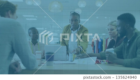 Collaborating six professionals reviewing fabric samples in studio with laptop, measuring tape 135624940