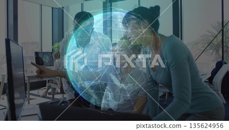 Team wearing formal attire collaborating around monitor in office, with digital globe overlay 135624956