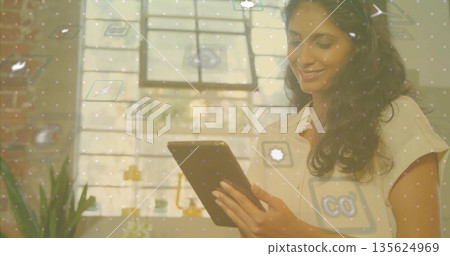 Smiling Indian student using tablet in office with potted plant, lamp, floating icons, copy space Smiling Indian student using tablet in office with potted plant, lamp, floating icons, copy space 135624969