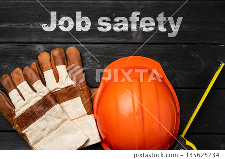Safety gear for construction work with gloves and helmet on a dark wooden surface Safety gear for construction work with gloves and helmet on a dark wooden surface 135625234