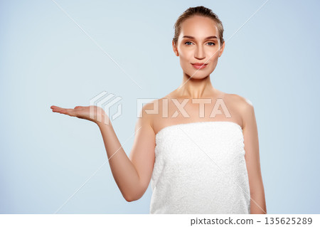 Woman in a white towel showing her palm in a light blue background indoors Woman in a white towel showing her palm in a light blue background indoors 135625289