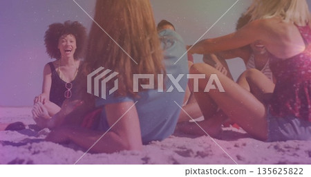 Laughing group of seven friends wearing swimwear chatting on sandy beach, with sunglasses, blanket Laughing group of seven friends wearing swimwear chatting on sandy beach, with sunglasses, blanket 135625822