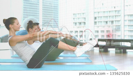 Three adults performing V-sit exercise on blue mats in fitness studio, wearing workout clothes 135625830