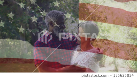 Embracing interracial couple sharing warm smiles in sunny garden with American flag overlay Embracing interracial couple sharing warm smiles in sunny garden with American flag overlay 135625834