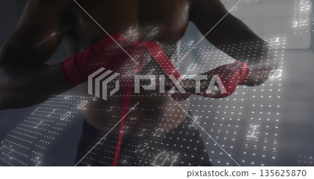 Wrapping shirtless boxer tightening red hand wraps inside gym room, with white binary code overlay 135625870