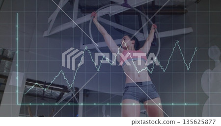 Hanging woman wearing pink sports bra, gray shorts arching from hoop in studio, with graph overlay Hanging woman wearing pink sports bra, gray shorts arching from hoop in studio, with graph overlay 135625877