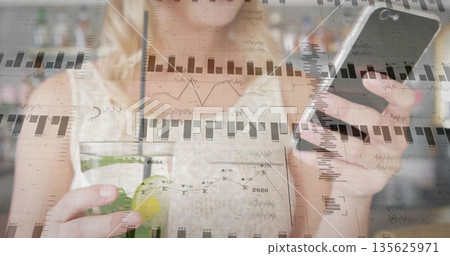 Sipping adult woman holding smartphone and analyzing overlay charts in kitchen, with smoothie jar Sipping adult woman holding smartphone and analyzing overlay charts in kitchen, with smoothie jar 135625971