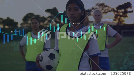 Soccer player holding black-and-white ball on grass field at dusk, with neon yellow training bibs 135625978