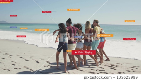 Walking group of seven friends along beach shoreline, with footprints and ocean waves 135625989