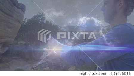 Exploring hiker extending clasped hands at canyon rim, with cliffs galactic lens flare copy space 135626016
