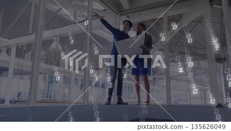 Two professionals wearing formal attire holding blueprint and pointing in unfinished building 135626049