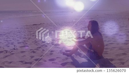 Sitting shirtless man in patterned trunks gazing at horizon on beach, with footprints, copy space Sitting shirtless man in patterned trunks gazing at horizon on beach, with footprints, copy space 135626070