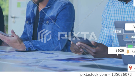 Two men analyzing charts and graphs in boardroom, with tablets laptop and digital overlay icons 135626073