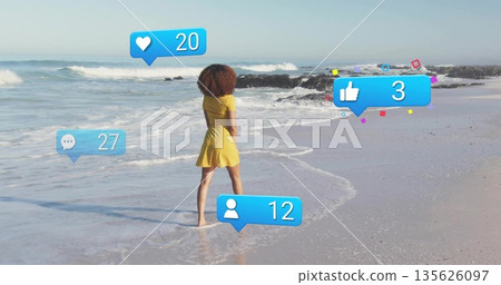 Standing solitary adult woman facing sandy ocean shore, displaying floating social media icons Standing solitary adult woman facing sandy ocean shore, displaying floating social media icons 135626097