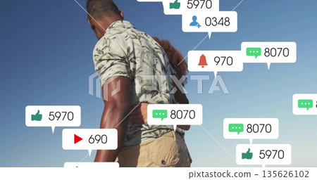 Hugging couple standing outdoors under clear blue sky, with floating social media icons Hugging couple standing outdoors under clear blue sky, with floating social media icons 135626102