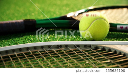 Resting yellow tennis ball nestling on overlapping racket strings over green turf court, copy space Resting yellow tennis ball nestling on overlapping racket strings over green turf court, copy space 135626108