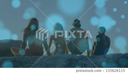 Sitting friends wearing board shorts and backwards cap on rocky ledge facing ocean, touching hands Sitting friends wearing board shorts and backwards cap on rocky ledge facing ocean, touching hands 135626115