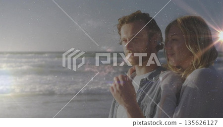 Gazing denim-clad man and sweater-clad woman on beach with waves sinking sun lens flare, copy space Gazing denim-clad man and sweater-clad woman on beach with waves sinking sun lens flare, copy space 135626127