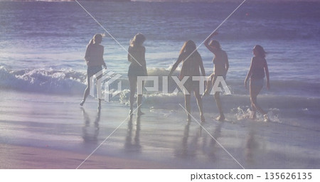 Standing five friends in summer clothes experiencing surf at beach, with ocean waves and wet sand Standing five friends in summer clothes experiencing surf at beach, with ocean waves and wet sand 135626135