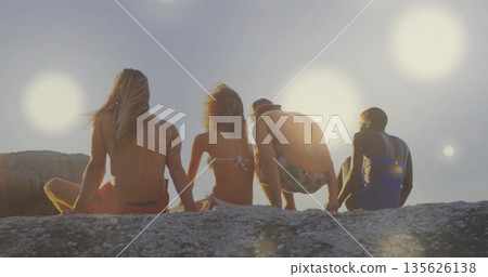 Sitting four friends gazing toward calm sea from rocky outcrop, with swimwear and bucket hat Sitting four friends gazing toward calm sea from rocky outcrop, with swimwear and bucket hat 135626138
