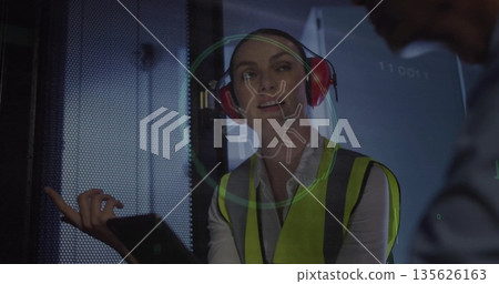 Gesturing vest and earmuff wearing technician tapping tablet in server room, with bug hologram Gesturing vest and earmuff wearing technician tapping tablet in server room, with bug hologram 135626163