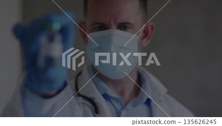 Holding medical vial, doctor wearing lab coat, surgical mask and gloves in clinic, with stethoscope 135626245
