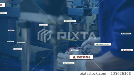 Gloved worker arms adjusting part under press in plant with labels, yellow-handled tool, copy space 135626308