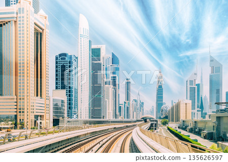 Metro road among glass skyscrapers in Dubai. Metropolitan railway among modern glass skyscrapers in Dubai. Traffic on street in Dubai. Urban background. Altered sky Metro road among glass skyscrapers in Dubai. Metropolitan railway among modern glass skyscrapers in Dubai. Traffic on street in Dubai. Urban background. Altered sky 135626597