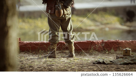 German Soldier Guards Mortar. Re-enactor Dressed As German Wehrmacht Infantry Soldier In World War Ii With Submachine Gun Mp 40 Patrols Territory Of Mortar Crew 135626664