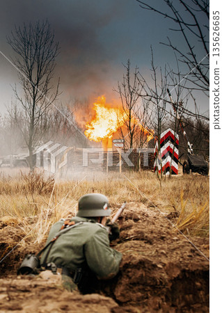 Re-enactors Dressed As World War Ii German Wehrmacht Infantry Soldiers Fighting Defensively In Trench. Defensive Position. Smokescreen. Building On Fire On Background 135626685