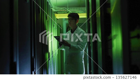 Reviewing tablet, Korean technician in lab coat inspecting racks with green lights in server room Reviewing tablet, Korean technician in lab coat inspecting racks with green lights in server room 135627146