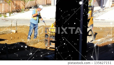 Using shovel, laborer in safety gear spreading soil beside loader at residential site, copy space 135627151