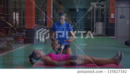 Blue-shirted trainer stretching client's leg on pink mat in gym, with line-graph overlays Blue-shirted trainer stretching client's leg on pink mat in gym, with line-graph overlays 135627162