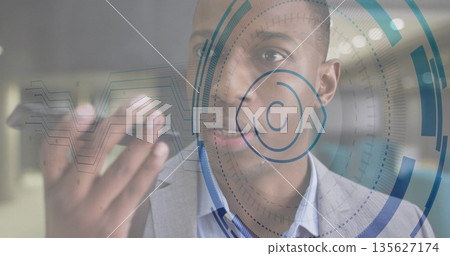 Businessman wearing suit interacting with AR graphics in office corridor, holding smartphone 135627174