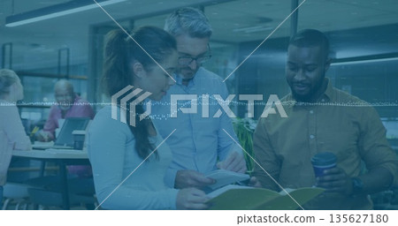 Office professionals reviewing printed documents in open-plan workspace, with binder and papers Office professionals reviewing printed documents in open-plan workspace, with binder and papers 135627180
