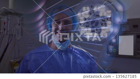 Standing surgeon wearing blue scrubs and mask in OR, with surgical light and molecular overlay Standing surgeon wearing blue scrubs and mask in OR, with surgical light and molecular overlay 135627185