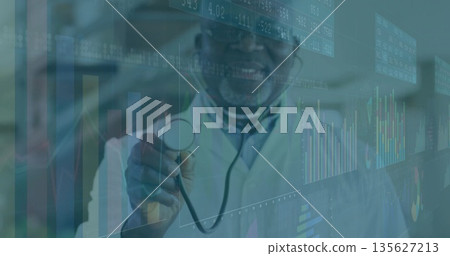 Senior physician wearing white coat and glasses holding stethoscope in clinic, with digital charts Senior physician wearing white coat and glasses holding stethoscope in clinic, with digital charts 135627213