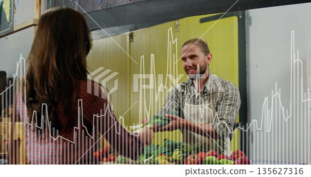 Apron-clad vendor handing leafy greens to customer in market stall, with crates of fresh vegetables 135627316