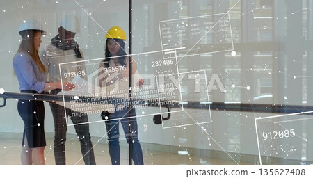 Reviewing architects wearing safety helmets examining blueprints at glass railing, with data panels 135627408