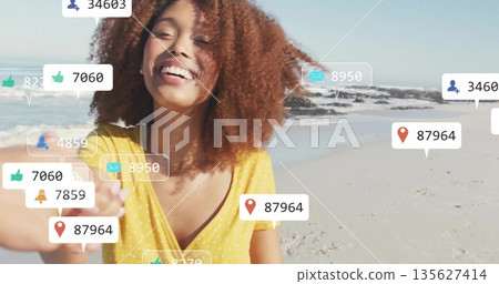 Creator wearing blouse holding smartphone taking selfie on beach with floating social media icons Creator wearing blouse holding smartphone taking selfie on beach with floating social media icons 135627414