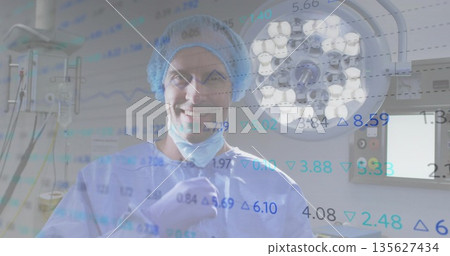 Surgeon wearing blue scrubs reviewing monitors under surgical light in OR, stock data overlay Surgeon wearing blue scrubs reviewing monitors under surgical light in OR, stock data overlay 135627434