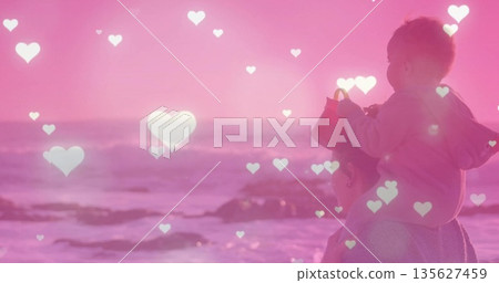 Standing mother and baby boy gazing at shoreline, with red bucket and heart overlays, copy space 135627459