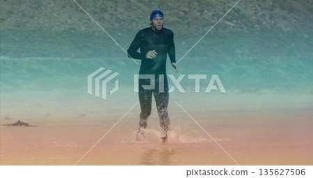 Athlete in black wetsuit running onto rocky lakeshore from shallow water, with swim cap and goggles Athlete in black wetsuit running onto rocky lakeshore from shallow water, with swim cap and goggles 135627506