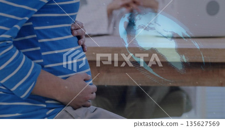 Sitting pregnant woman cradling abdomen in clinic, with wooden desk, laptop, holographic globe Sitting pregnant woman cradling abdomen in clinic, with wooden desk, laptop, holographic globe 135627569